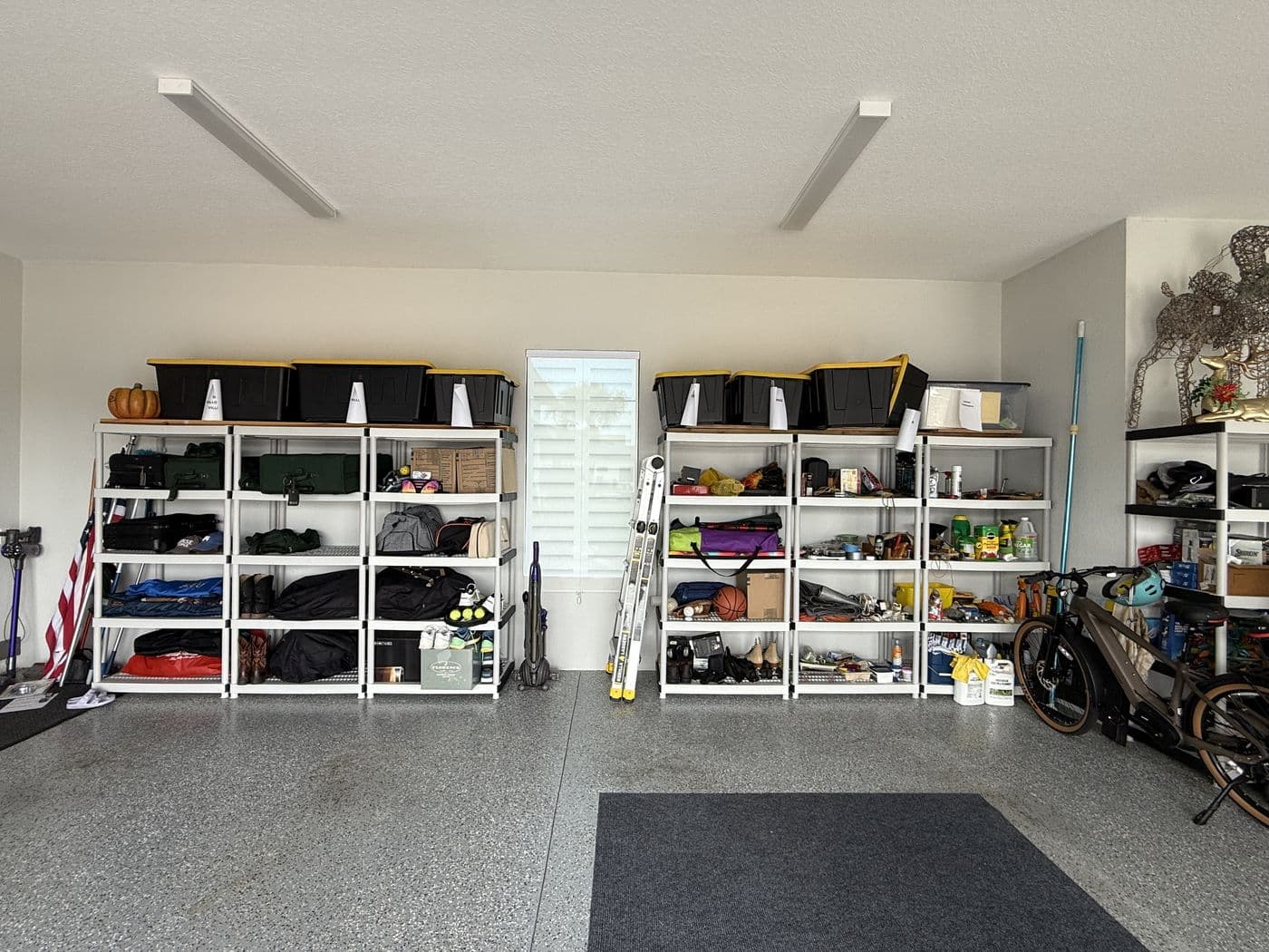 Before, a garage lined with open wire shelving full of bins, bags and sports gear.