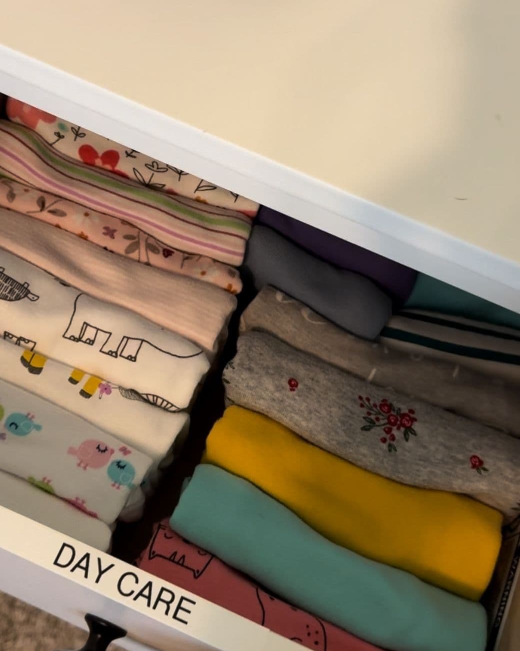 A white drawer labeled DAY CARE with small folded clothes standing in two neat rows.