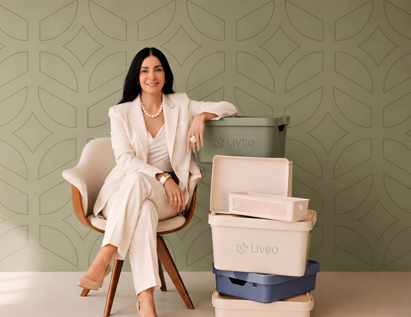 Silvana Buranek, founder of LIVBO, seated in a cream suit beside a stack of LIVBO storage bins in sage, cream and blue.