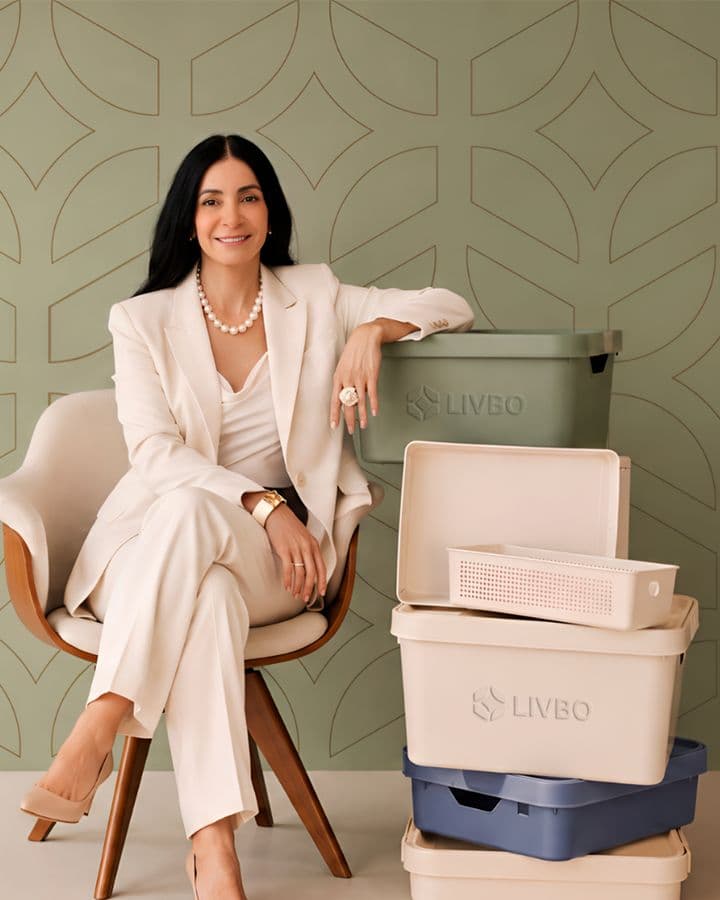 Silvana Buranek, founder of LIVBO, seated in a cream suit beside a stack of LIVBO storage bins in sage, cream and blue.