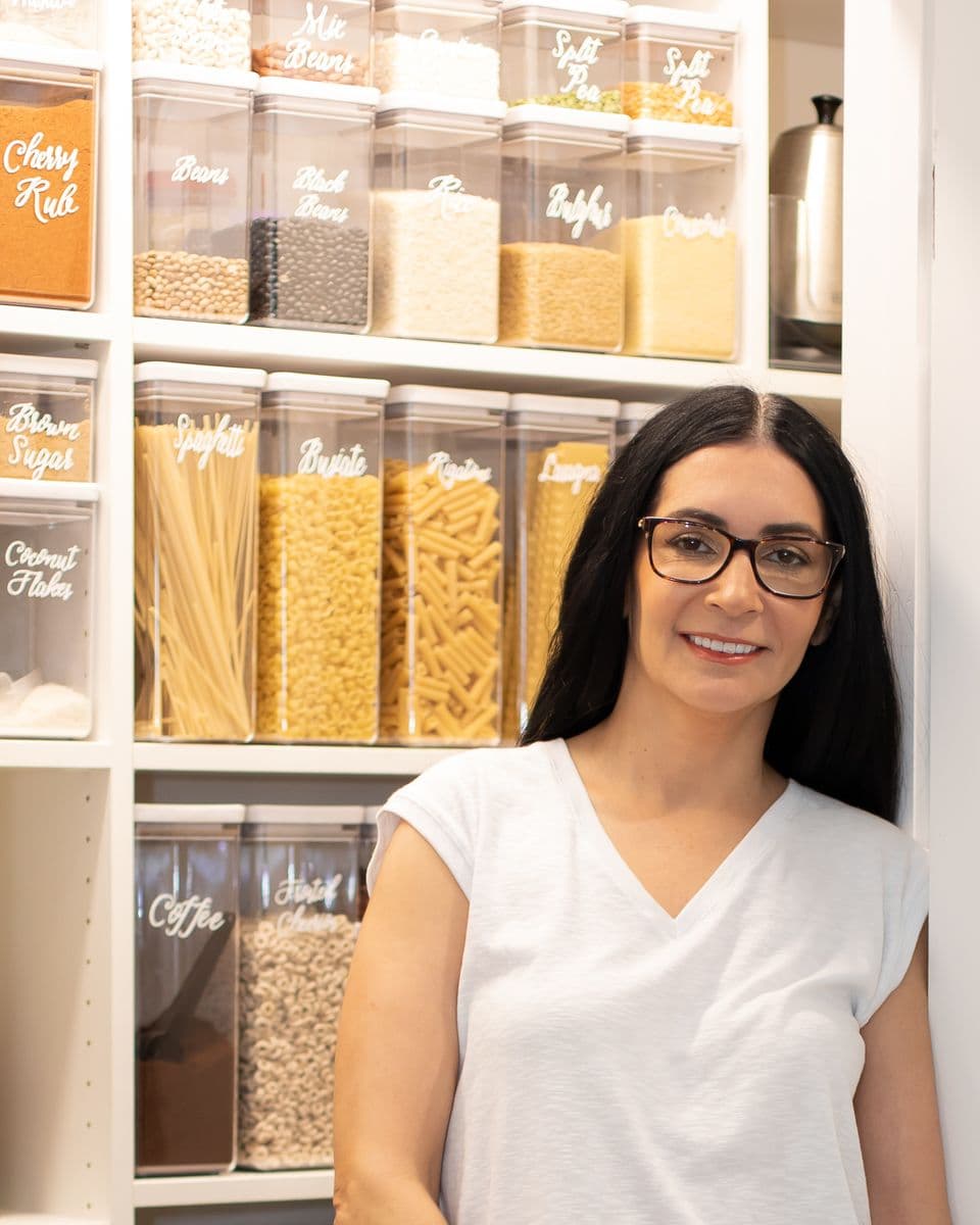 Silvana stands in a finished built in pantry, shelves lined with clear containers labeled by hand.